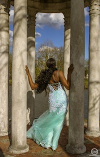 a woman in a blue dress is leaning against a pillar